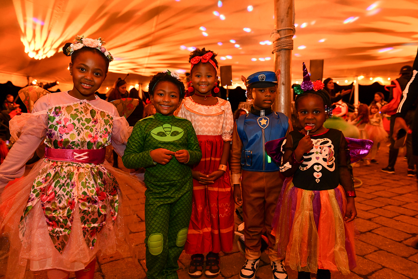 A group of costumed children smile under an orange tent at Boo at the Zoo.