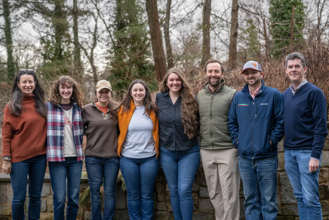 Photo of five women and three men standing together for a photo. The people are all smiling and standing close to one another.