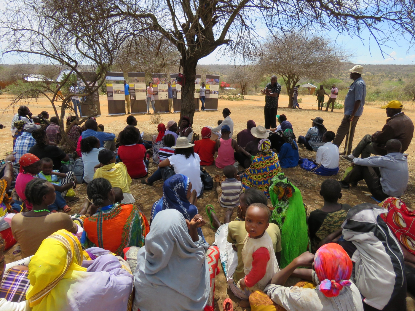 Community members in Laikipia County, Kenya, sit outside as someone gives a presentation on exhibit panels from the mobile Outbreak DIY exhibit.