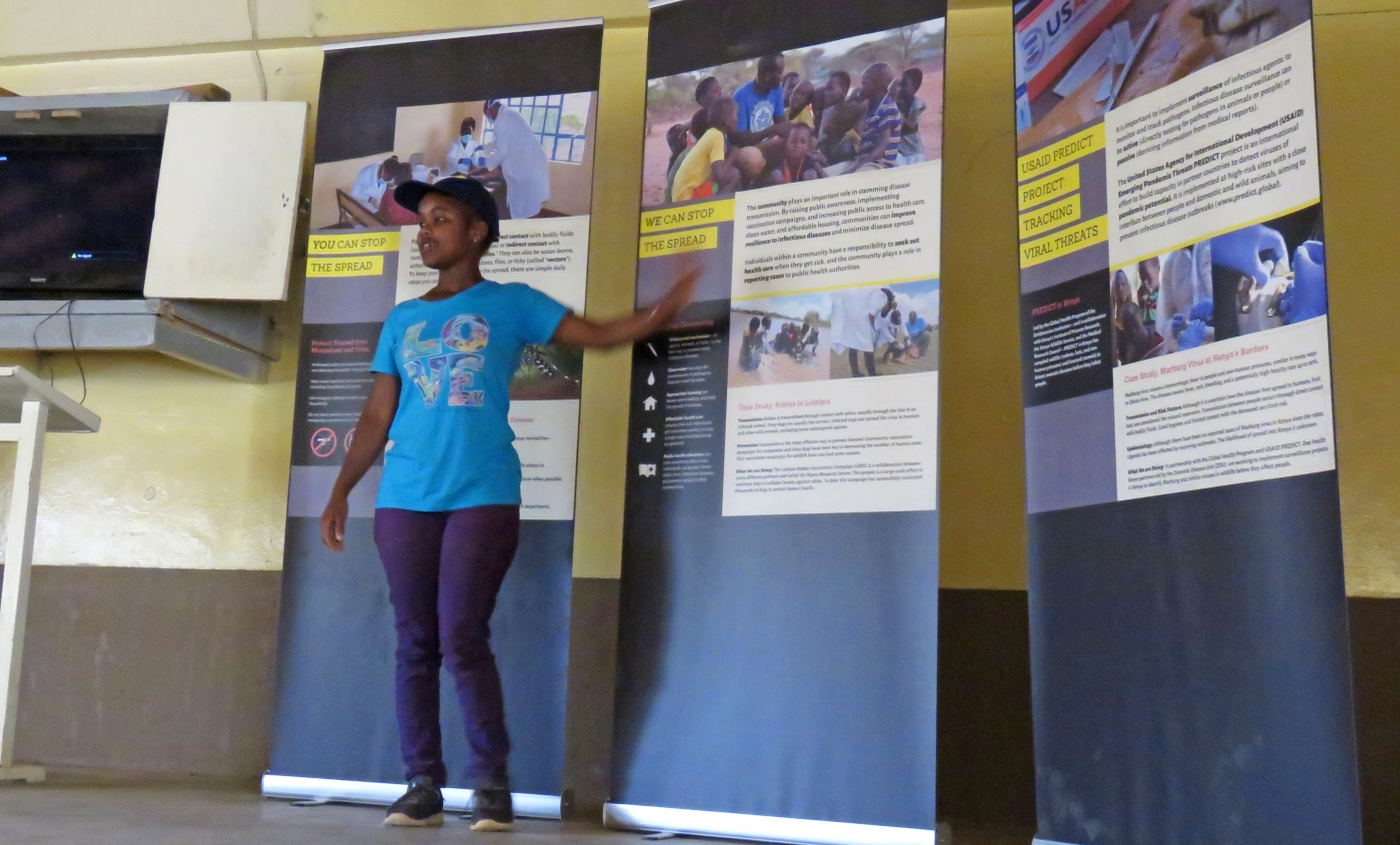 Public health graduate student Caroline Cherotich Mutai gives a presentation on the mobile Outbreak DIY exhibit. She is standing in front of the mobile exhibit panels and points to one as she speaks.