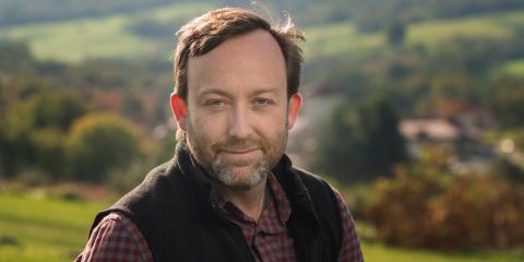 Headshot of Tom Akre with a green, hilly landscape in the background