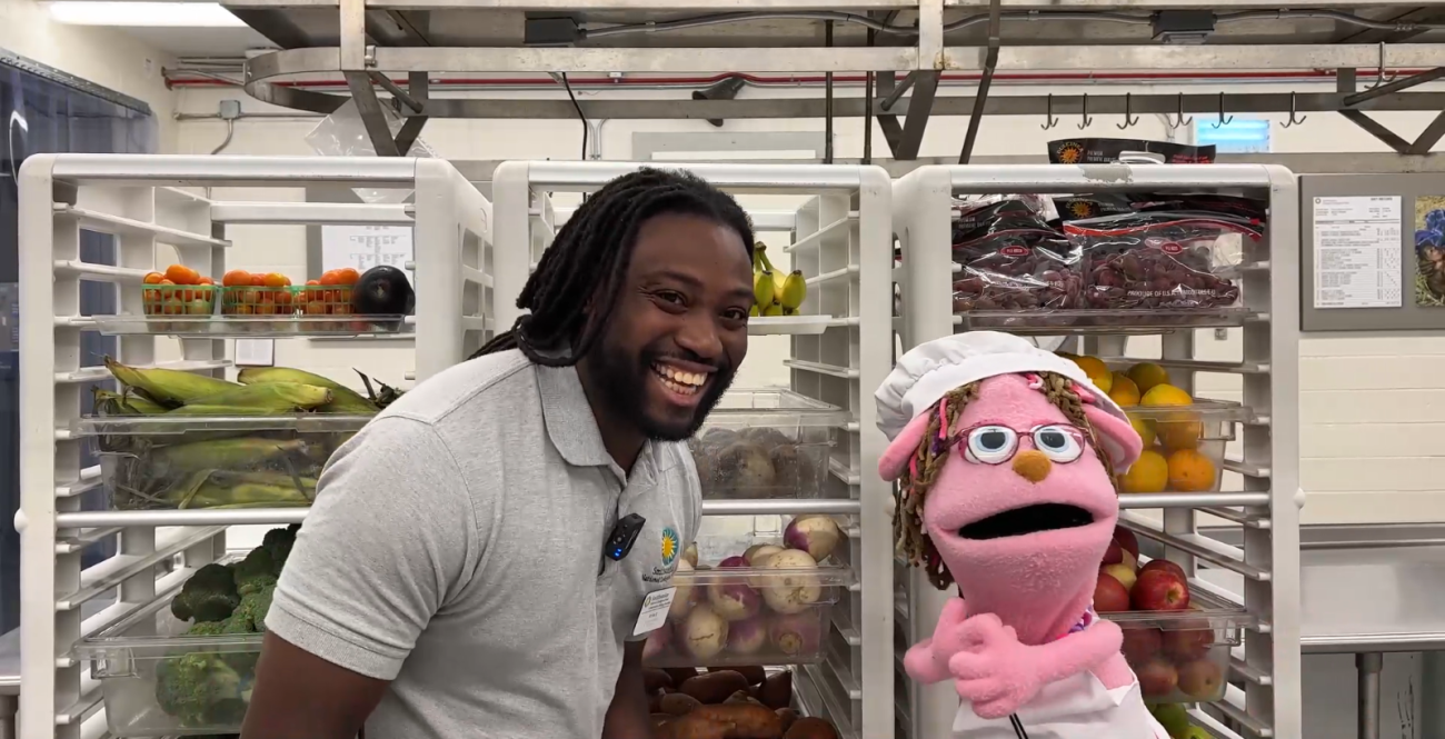 A smiling keeper stands on the left next to a pink jackalope puppet.