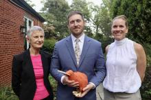 Photo of two women and a man standing together smiling. The people are all wearing formal clothing and the man holds a toy kiwi bird in his hands.