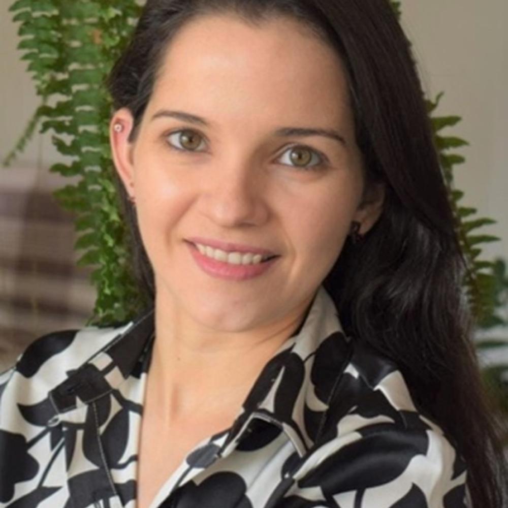 A dark-haired woman smiles in front of a fern in an office setting.