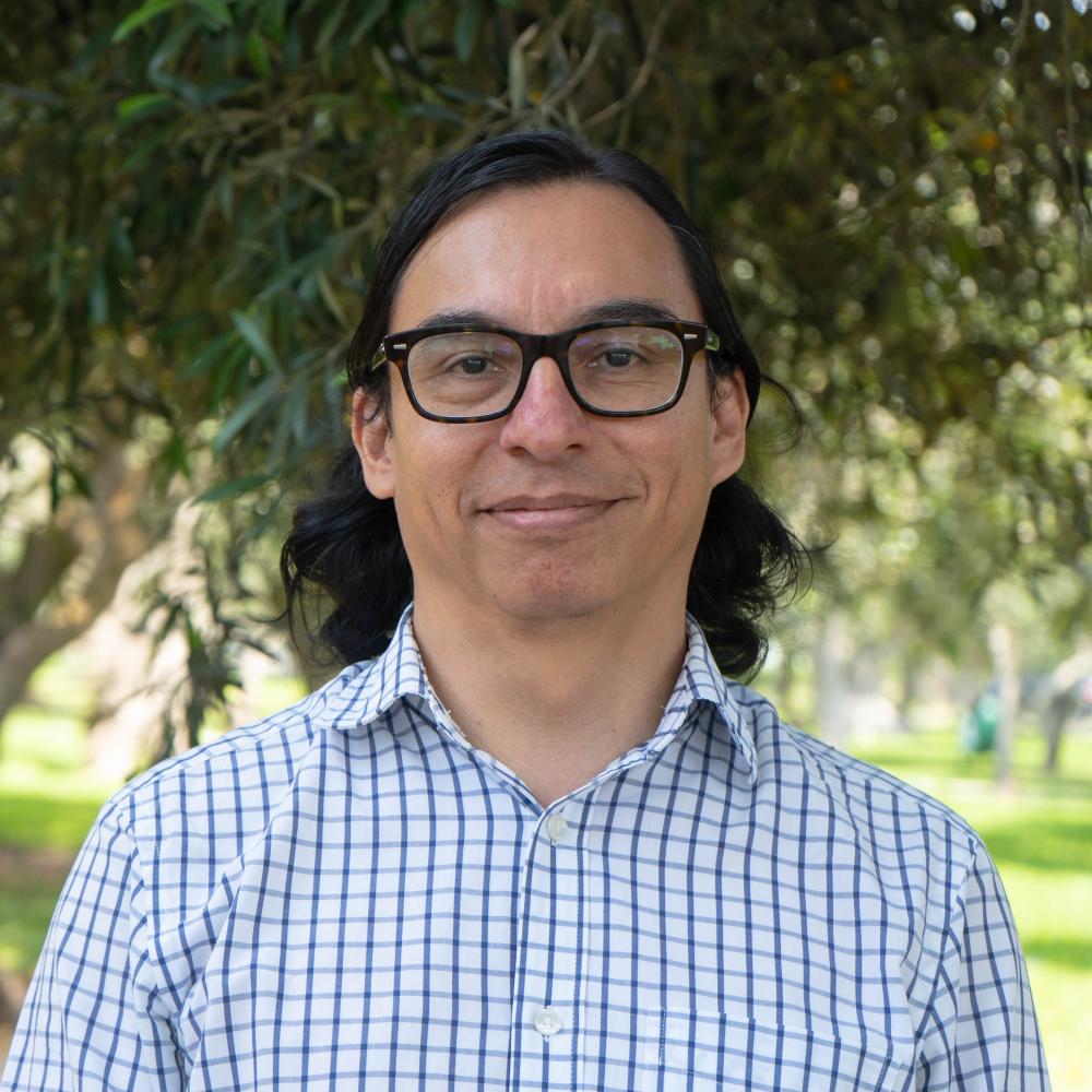 Headshot of a man with glasses in front of a lush tree.