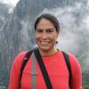 A dark-haired woman in a bright colored orange shirt smiles with a misty mountain landscape behind her.