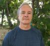 A white-haired scientist poses for a headshot with tropical trees behind him.