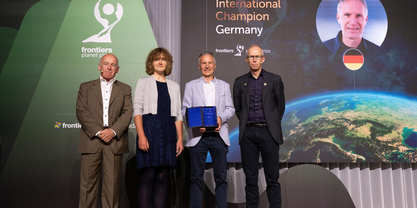 A woman and three men stand on a stage to accept an award. In the background, text on a screen reads, "2024 International Champion: Germany"