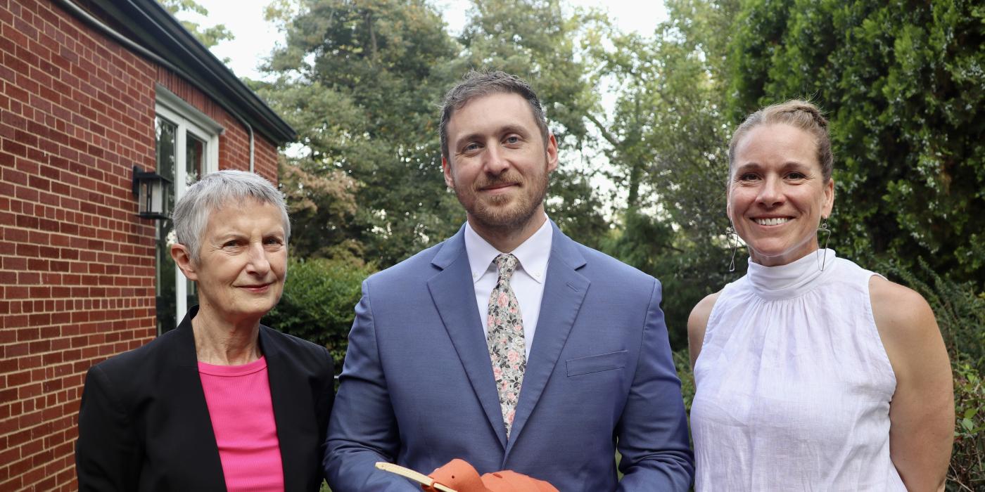 Photo of two women and a man standing together smiling. The people are all wearing formal clothing and the man holds a toy kiwi bird in his hands.